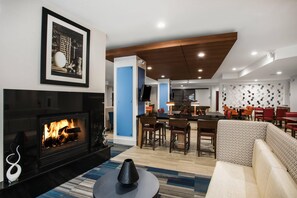 A modern living room with a fireplace, a dining area with chairs, and a kitchen in the background. - Country Inn & Suites by Radisson, Downtown Albany New York (Albany)