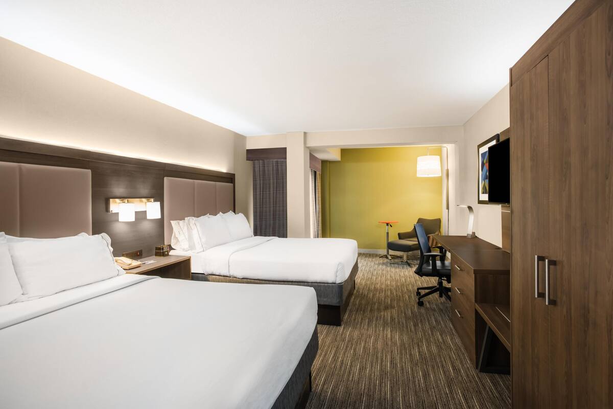 A hotel room with two beds, a desk, a chair, a TV, and a wardrobe.