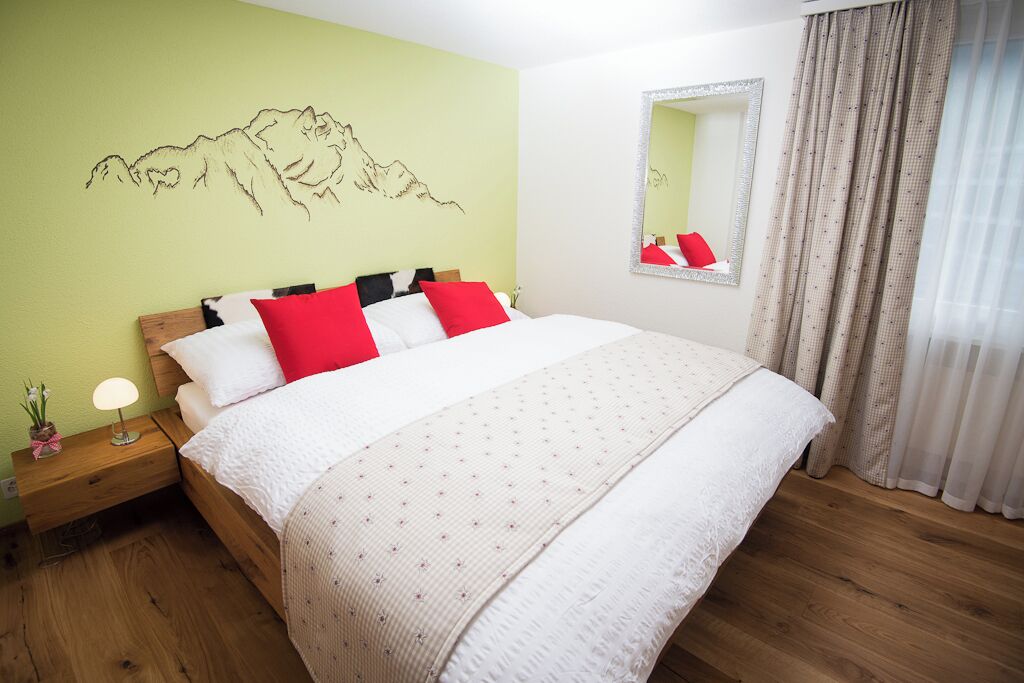 A bedroom with a bed, a nightstand, a mirror, and a mountain mural on the wall.