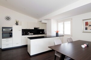 Una cocina moderna con armarios blancos, encimera negra y una zona de comedor con mesa de madera.
