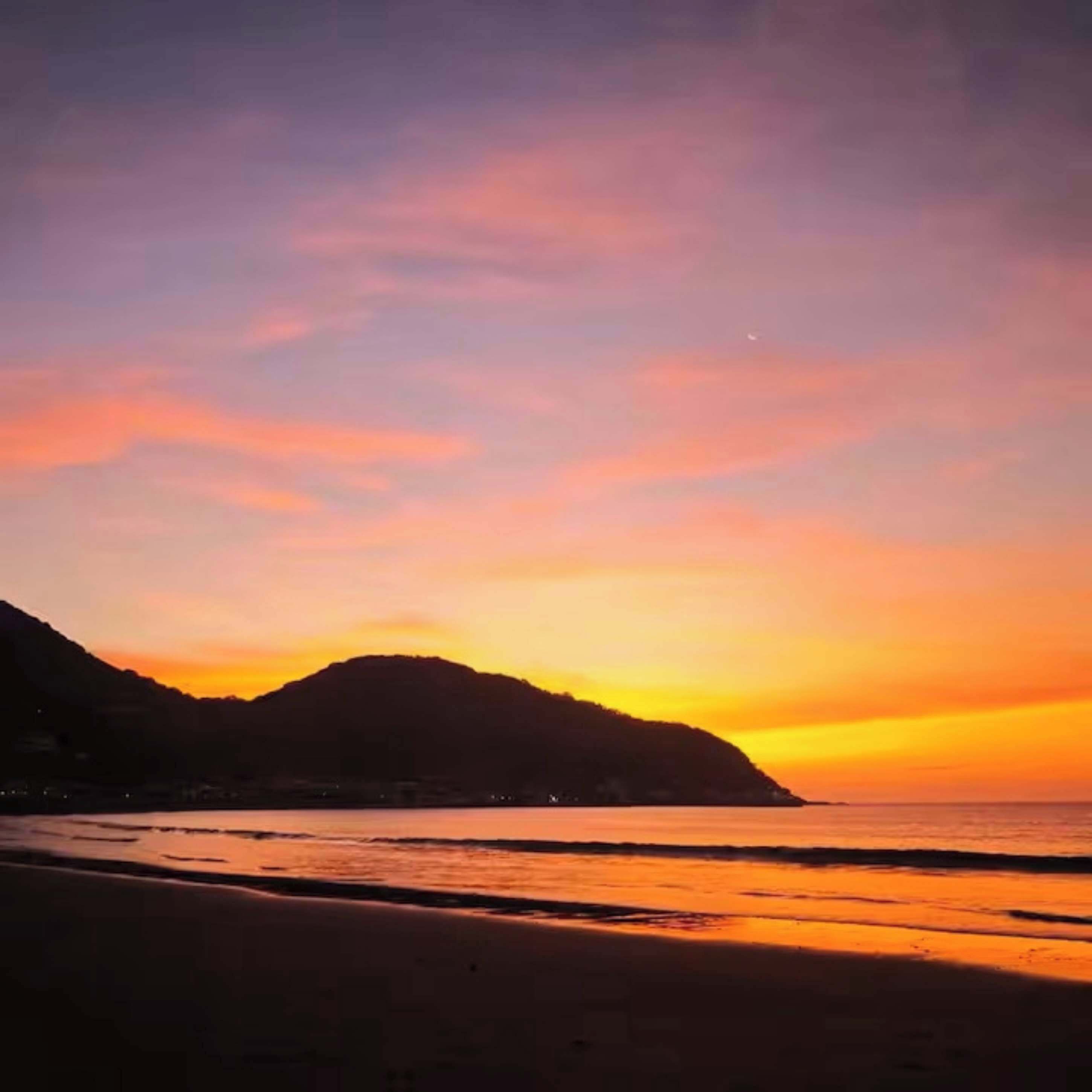 A sunset over a beach with a mountain in the background.