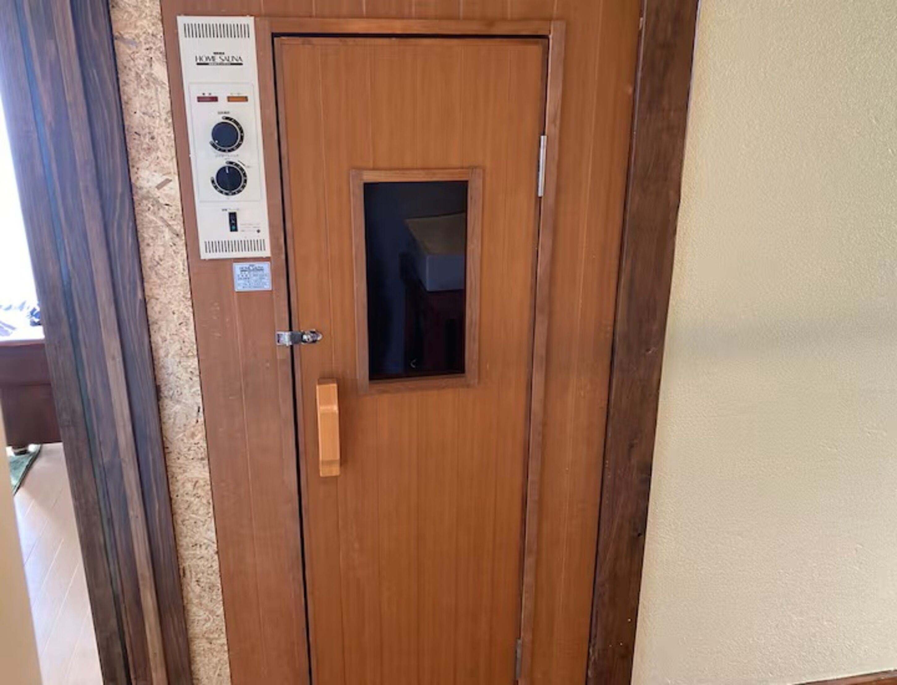 A wooden door with a small window, a doorbell, and a control panel with dials and buttons.