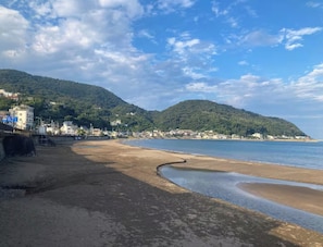 A beach with a curved shoreline, buildings on a hillside, and a clear sky. - IG3 Oyado Sankanshion (Ito)
