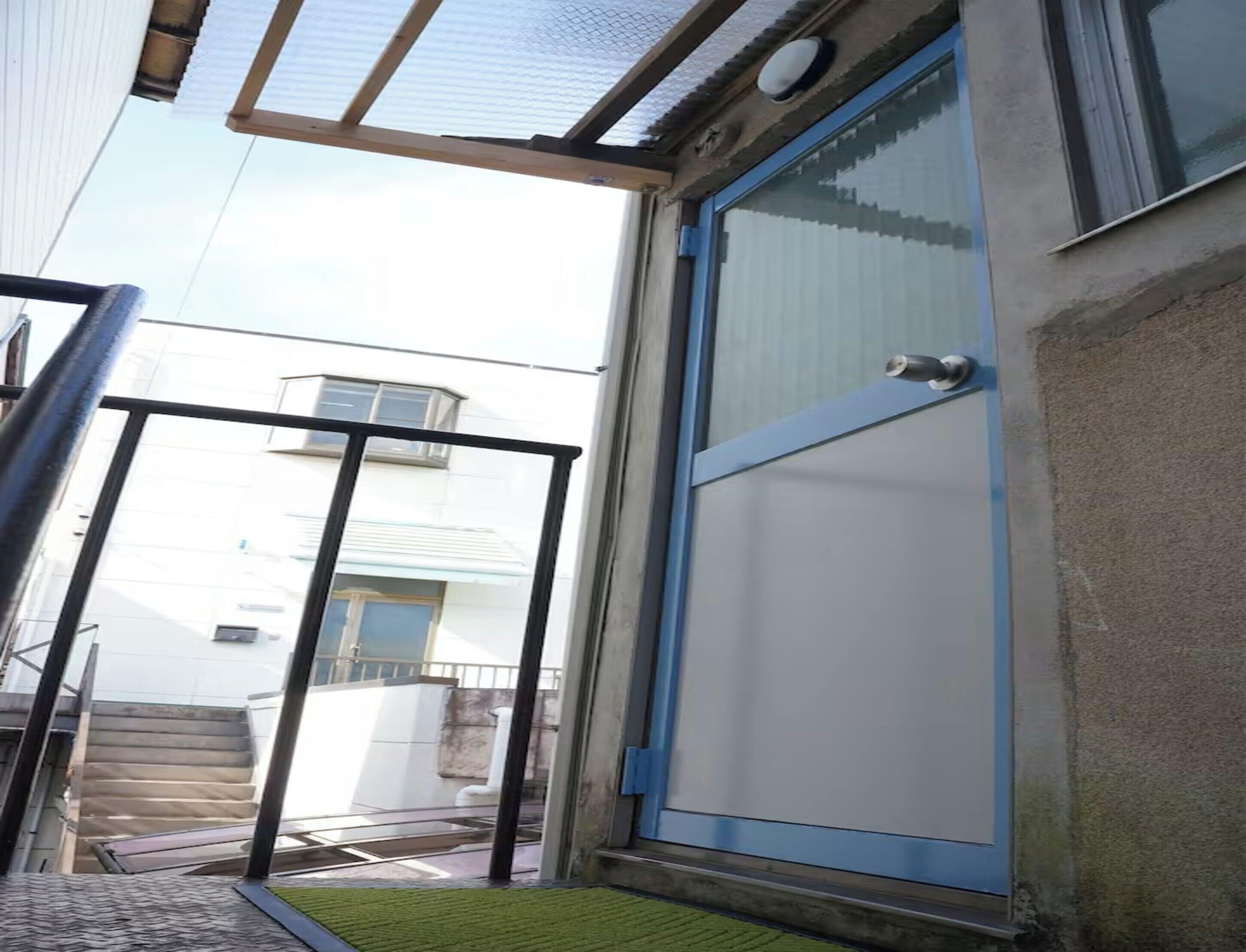 A modern building with a glass door and a metal gate, a staircase, and a clear view of a neighboring building.