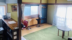 Una habitación con techo de madera, un escritorio con silla, una mesita y un ventanal con cortinas.