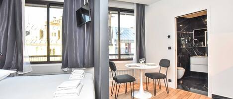A modern hotel room with a large bed, a round table with chairs, a TV, and a bathroom with a black marble sink.