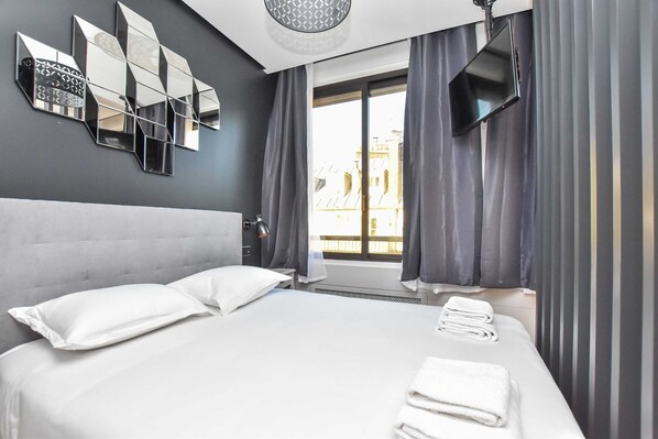 A modern hotel room with a large bed, a flat-screen TV, and a view of the city through the window. - Chic studio w/ jacuzzi - 2P - near Palais Garnier (Paris)