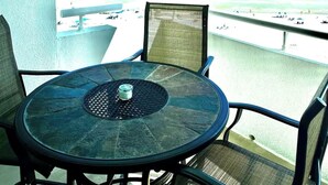 A round table with chairs on a balcony overlooking a beach with people and a boat in the distance.