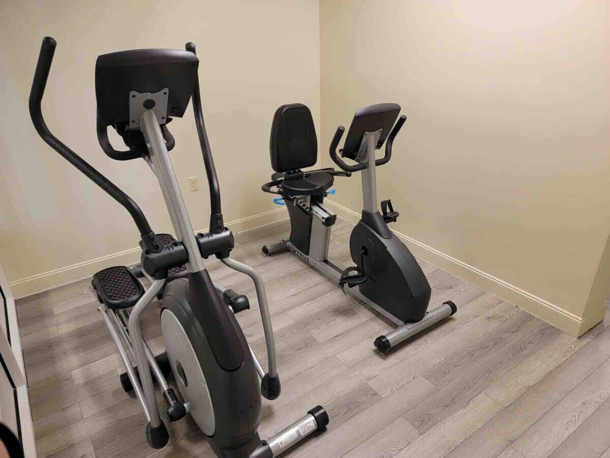 Two stationary bikes in a room with wooden flooring and beige walls.