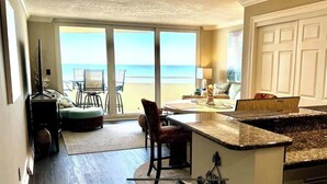 A kitchen with a large island, a dining area with a view of the beach, and a sliding glass door leading to the patio.