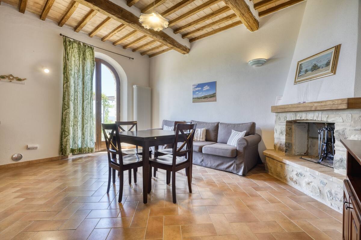 Un comedor con una mesa y sillas, un sofá, una chimenea y vistas a través de una ventana.