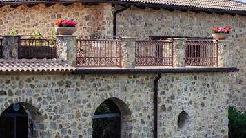A stone building with a tiled roof, arched windows, and a balcony with flower pots.