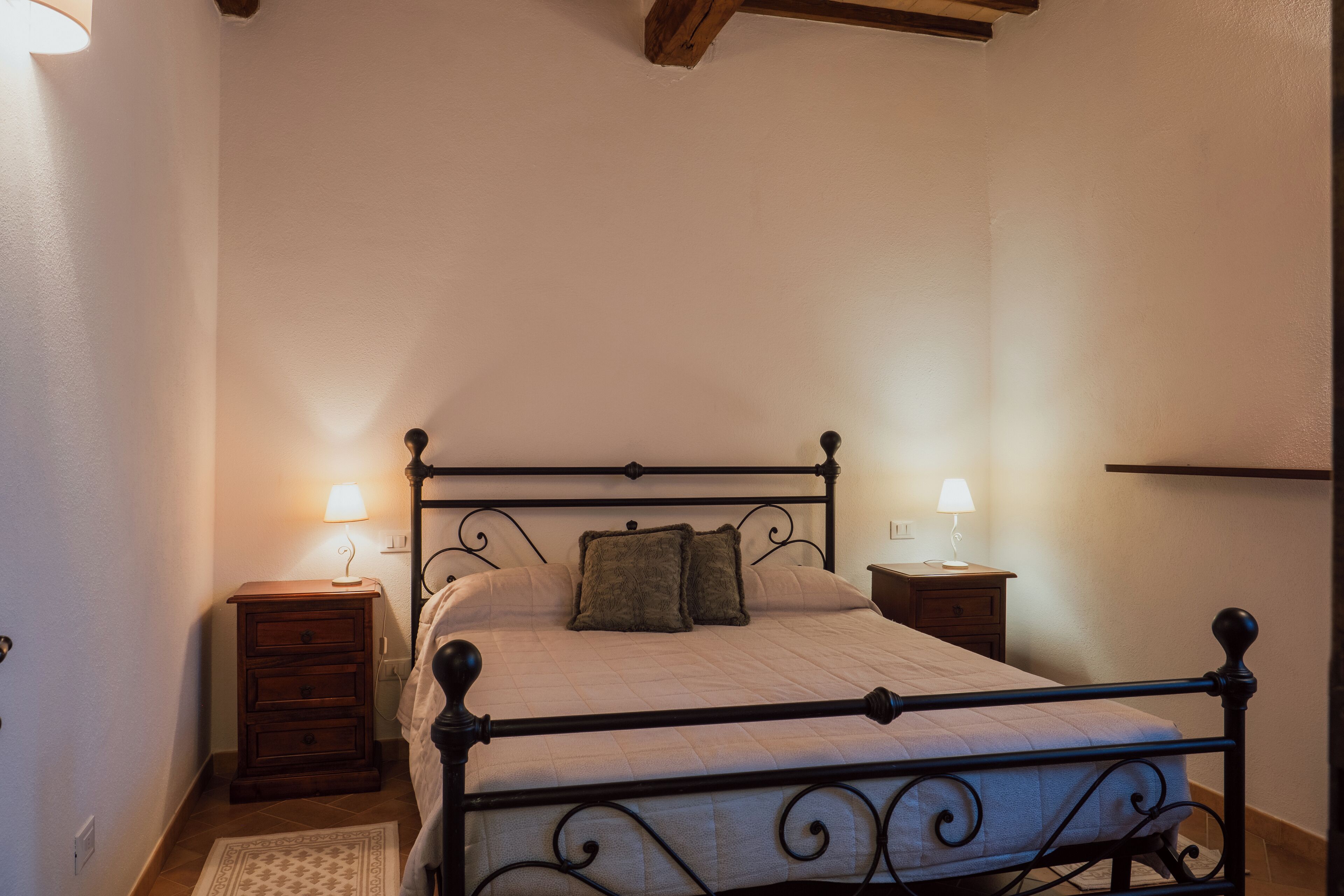 Quarto com cama, duas mesas de cabeceira com luminárias, um criado-mudo de madeira e um tapete estampado.