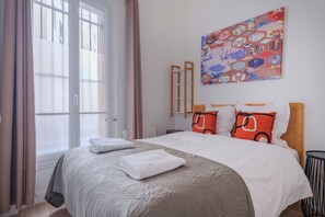 A neatly made bed with white linens, a colorful abstract painting on the wall, and a window with curtains. - Paris Expo Residence (Paris)