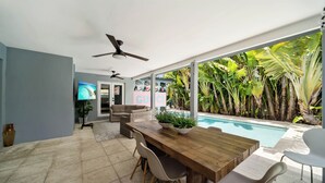 A modern living room with a wooden dining table, two sofas, and a poolside view. - Perfect Location, 6 Bedrooms, 11 Beds, & The Pool -- Welcome to the Gucci House! (Miami)