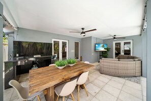 Enjoy meals at the dining table surrounded by comfortable chairs, a flat-screen TV, and a wicker sofa.