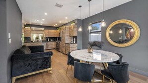 A modern kitchen with dark grey walls, wooden cabinets, and a marble dining table with black chairs. - Perfect Location, 6 Bedrooms, 11 Beds, & The Pool -- Welcome to the Gucci House! (Miami)