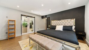 A modern bedroom with a large bed, a bench, a wardrobe, and a sliding glass door leading to a balcony. - Perfect Location, 6 Bedrooms, 11 Beds, & The Pool -- Welcome to the Gucci House! (Miami)