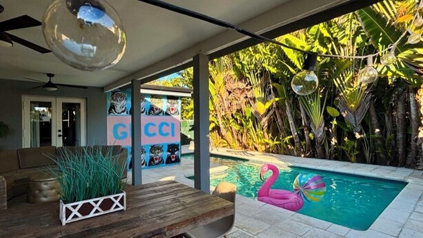 A pool area with a flamingo float, a tiki bar, and lush tropical plants. - Perfect Location, 6 Bedrooms, 11 Beds, & The Pool -- Welcome to the Gucci House! (Miami)