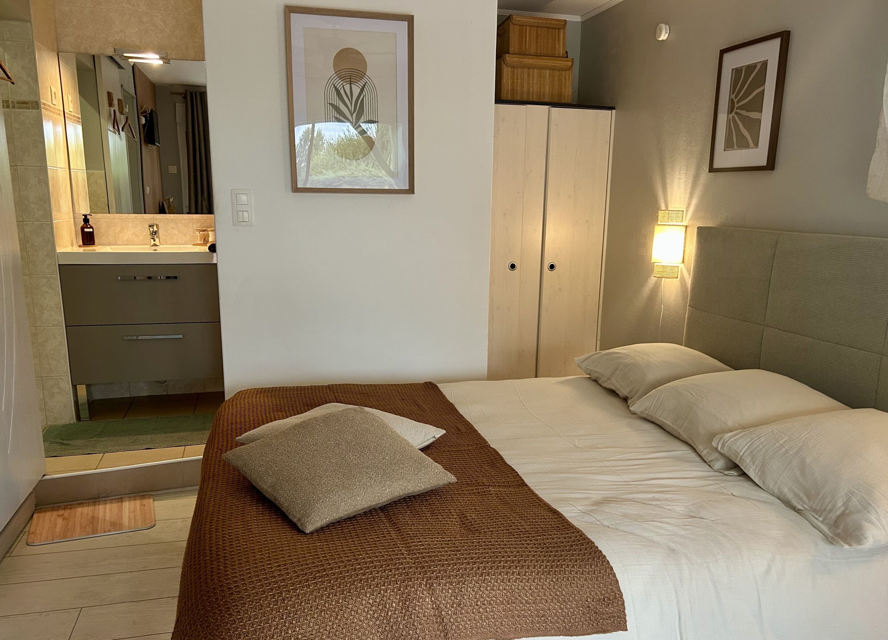 A bedroom with a bed, pillows, a nightstand, a mirror, a wardrobe, and a framed picture on the wall.
