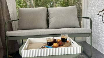 A green metal-framed sofa with two grey cushions, a white tray table with a glass of iced coffee, a pastry, and a spoon.
