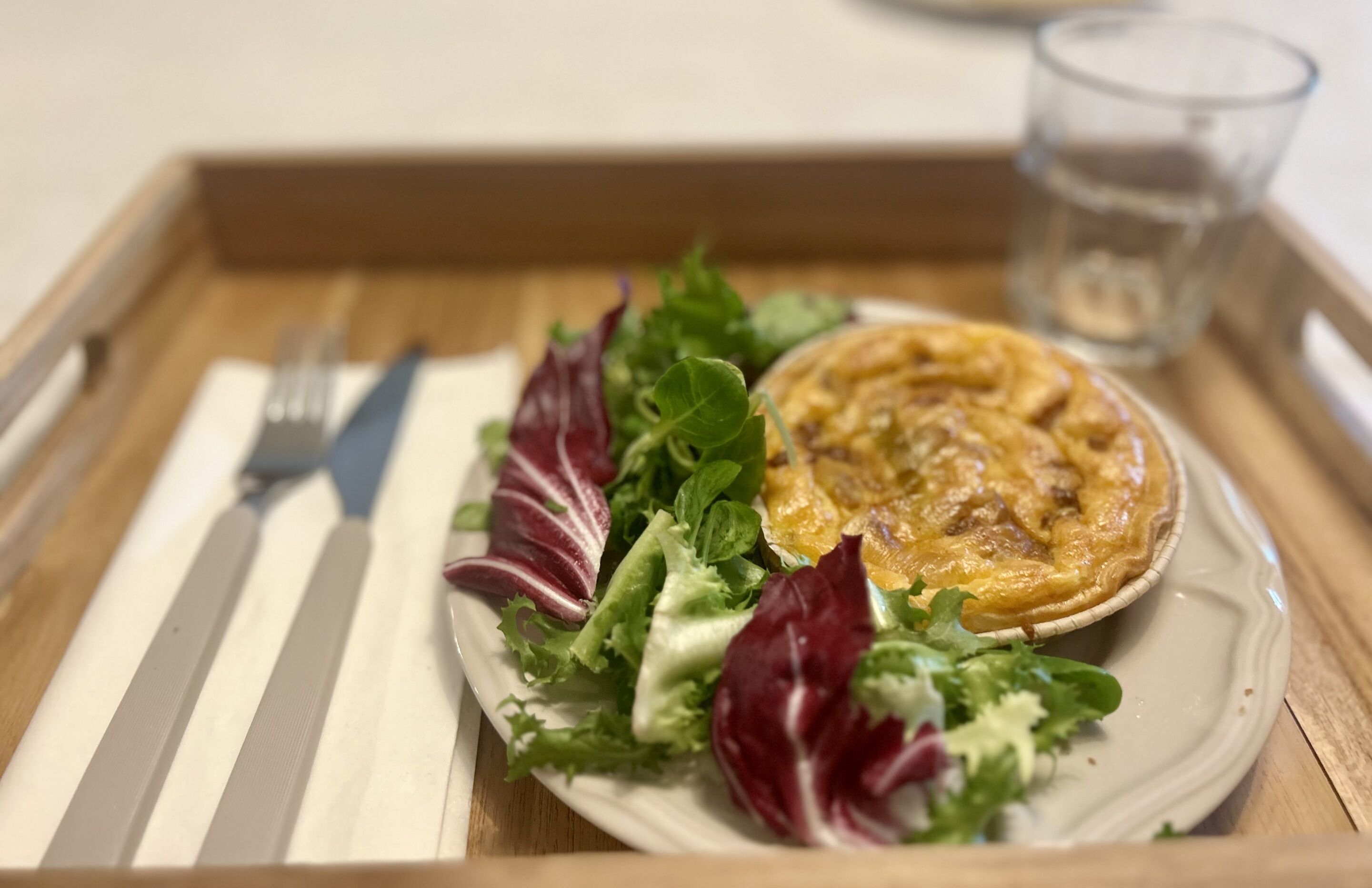 A tray with a plate of food, including a pie and salad, and a glass of water.