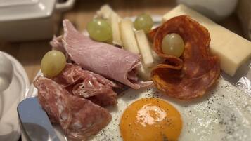 A breakfast plate with eggs, ham, salami, cheese, and grapes.