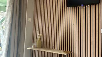 Une pièce avec un mur en bois à rayures, un téléviseur fixé au mur, une étagère avec un vase et un radiateur.