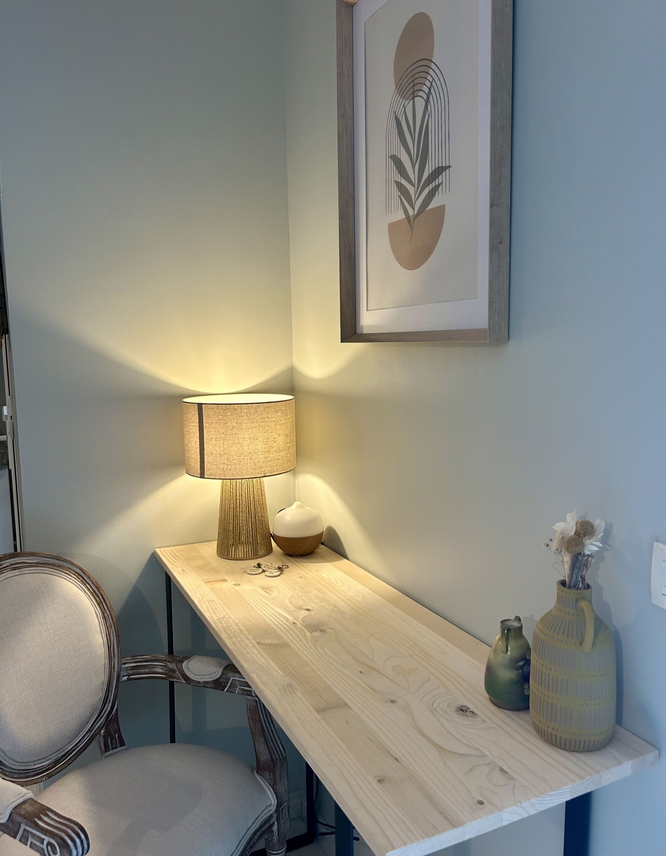 Un bureau en bois, une lampe, une chaise et deux vases sont disposés sur un mur.