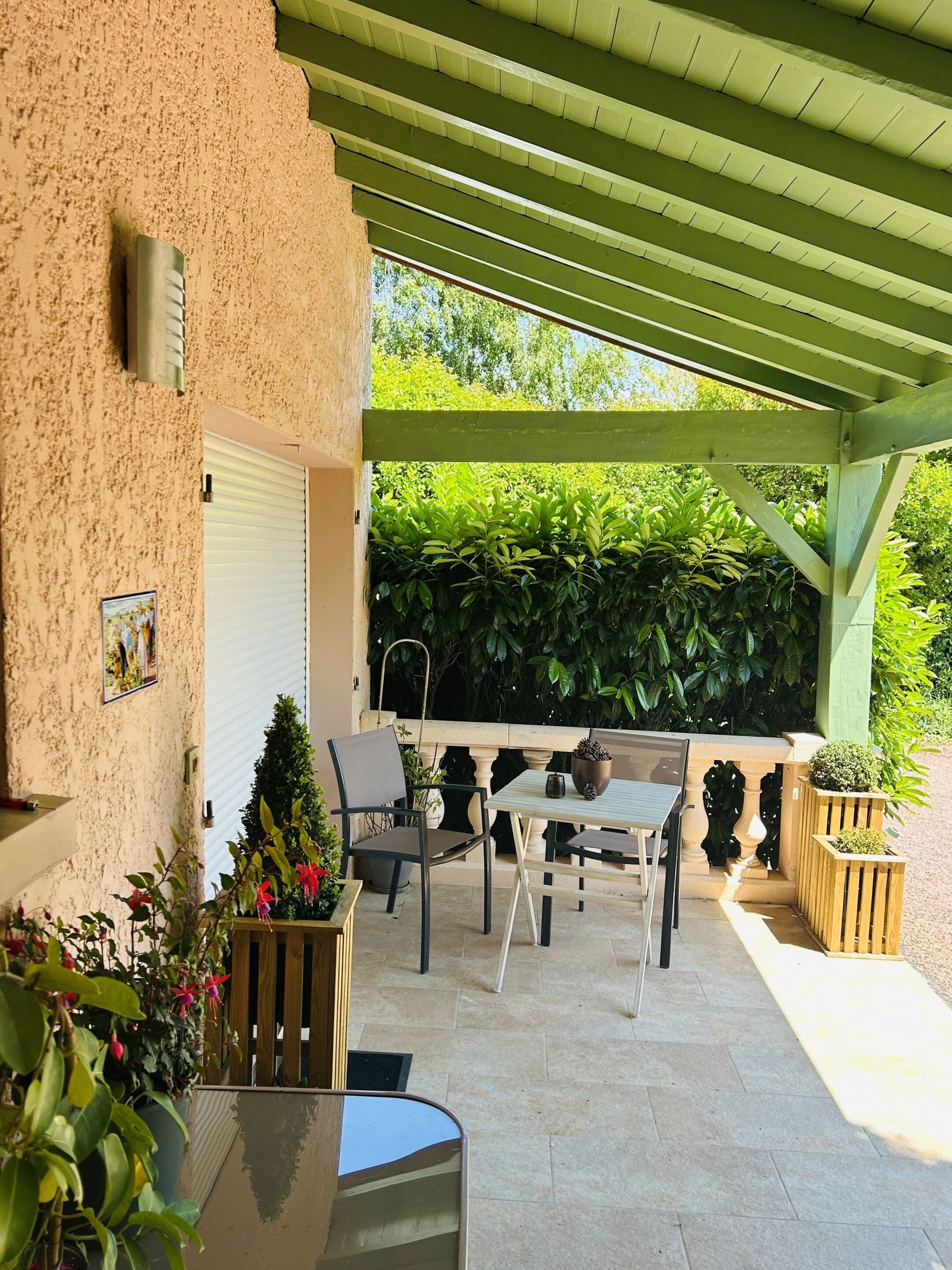 Une terrasse couverte avec une table et des chaises, entourée de plantes en pot et d’un mur végétal.