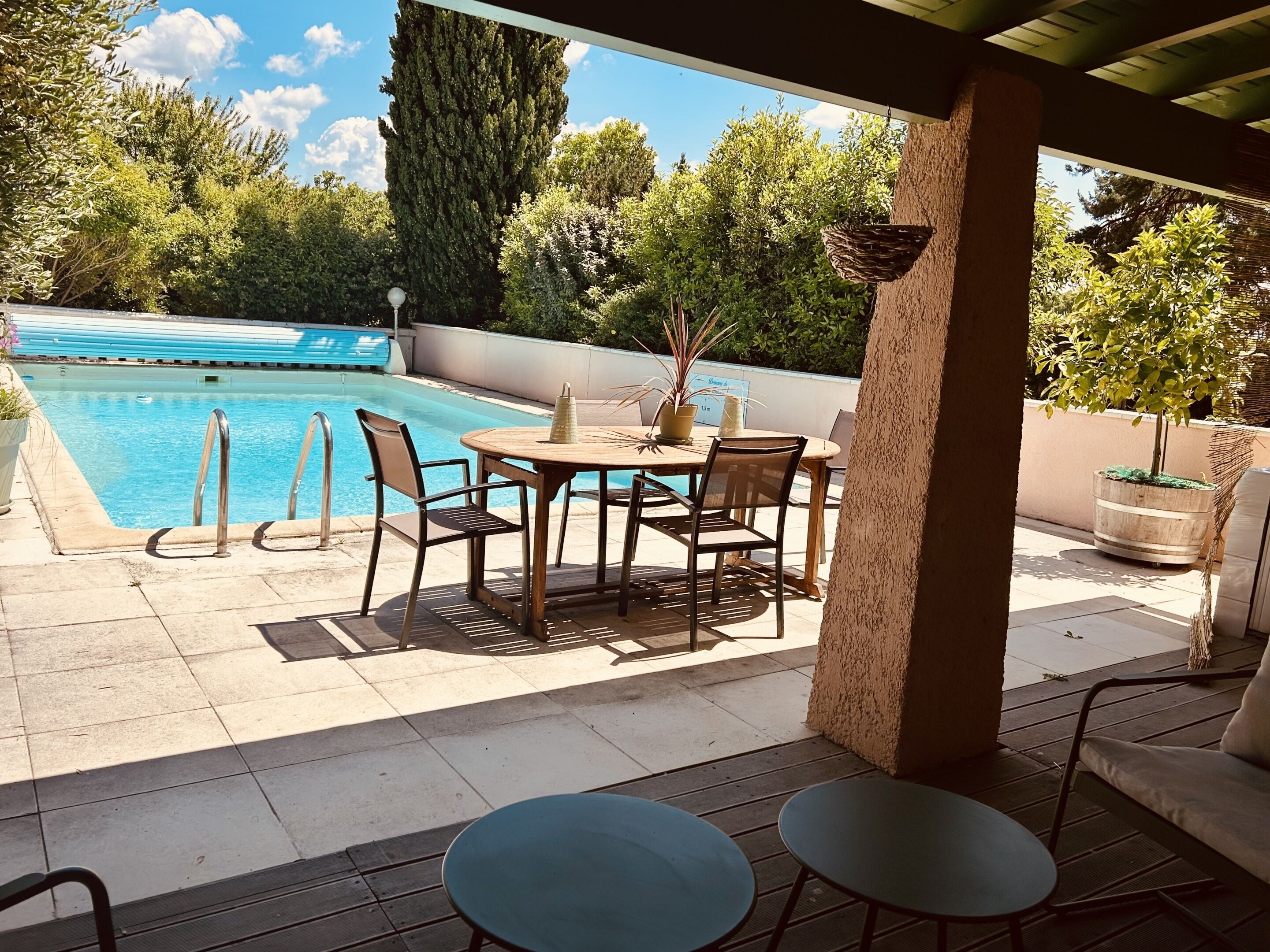 Un espace extérieur abrité comprenant une piscine, une table avec des chaises et une plante en pot.