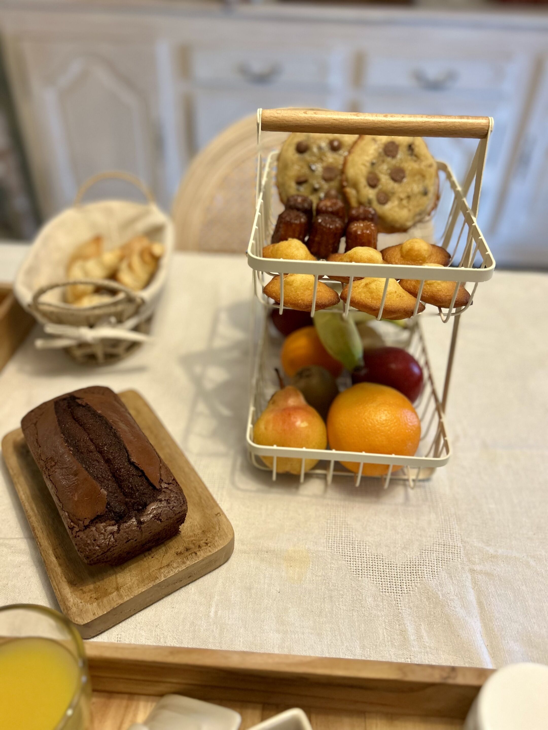 A tray with a loaf of bread, a basket of muffins, and a fruit bowl containing oranges and pears.