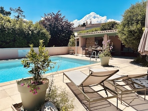 A swimming pool with lounge chairs and potted plants, a patio area with a table and chairs, and a building with a tiled roof in the background. - Demeure de L'estuaire (Plassac)