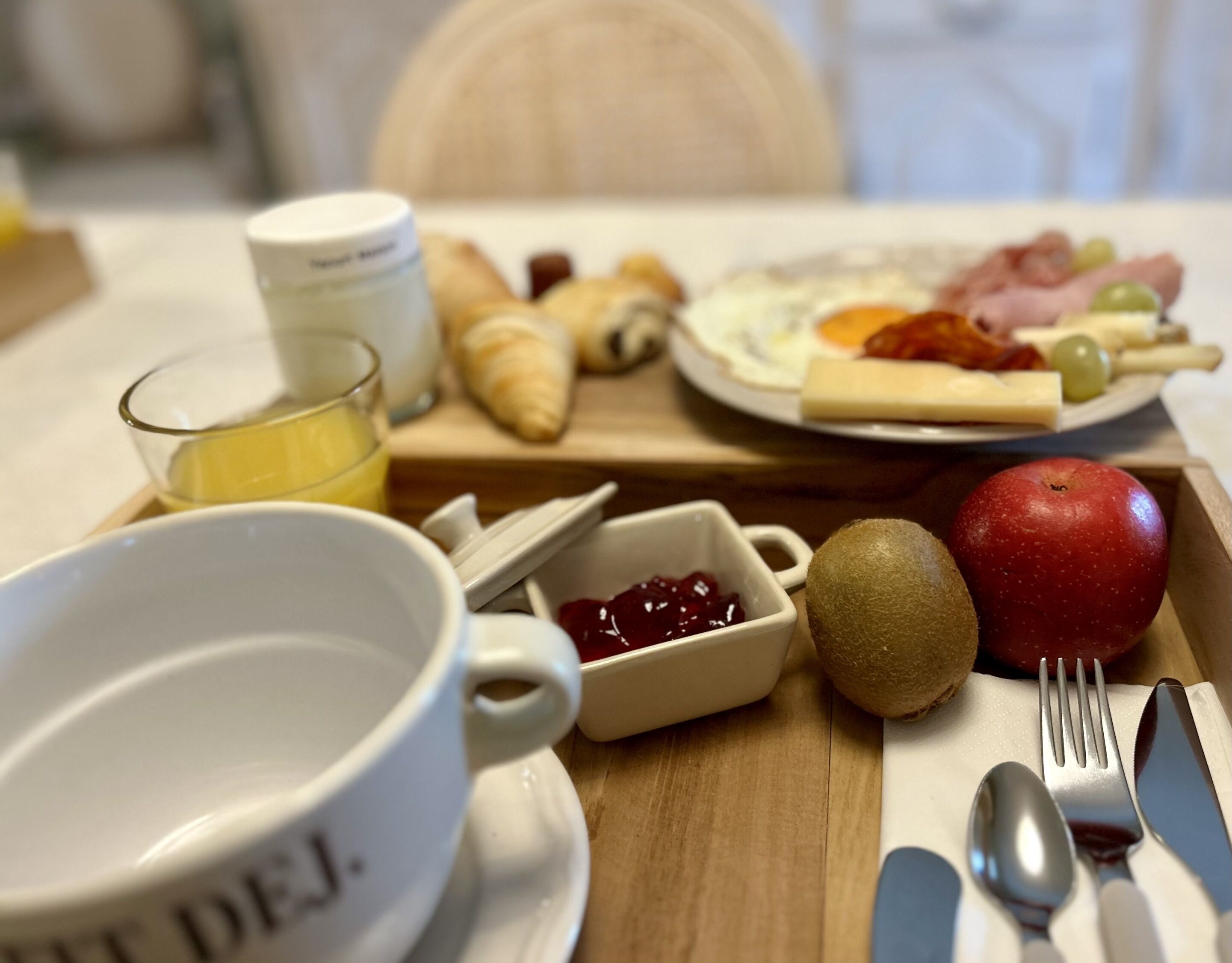 Une table mise pour le petit-déjeuner avec un croissant, une pomme et une assiette contenant des œufs et du jambon.