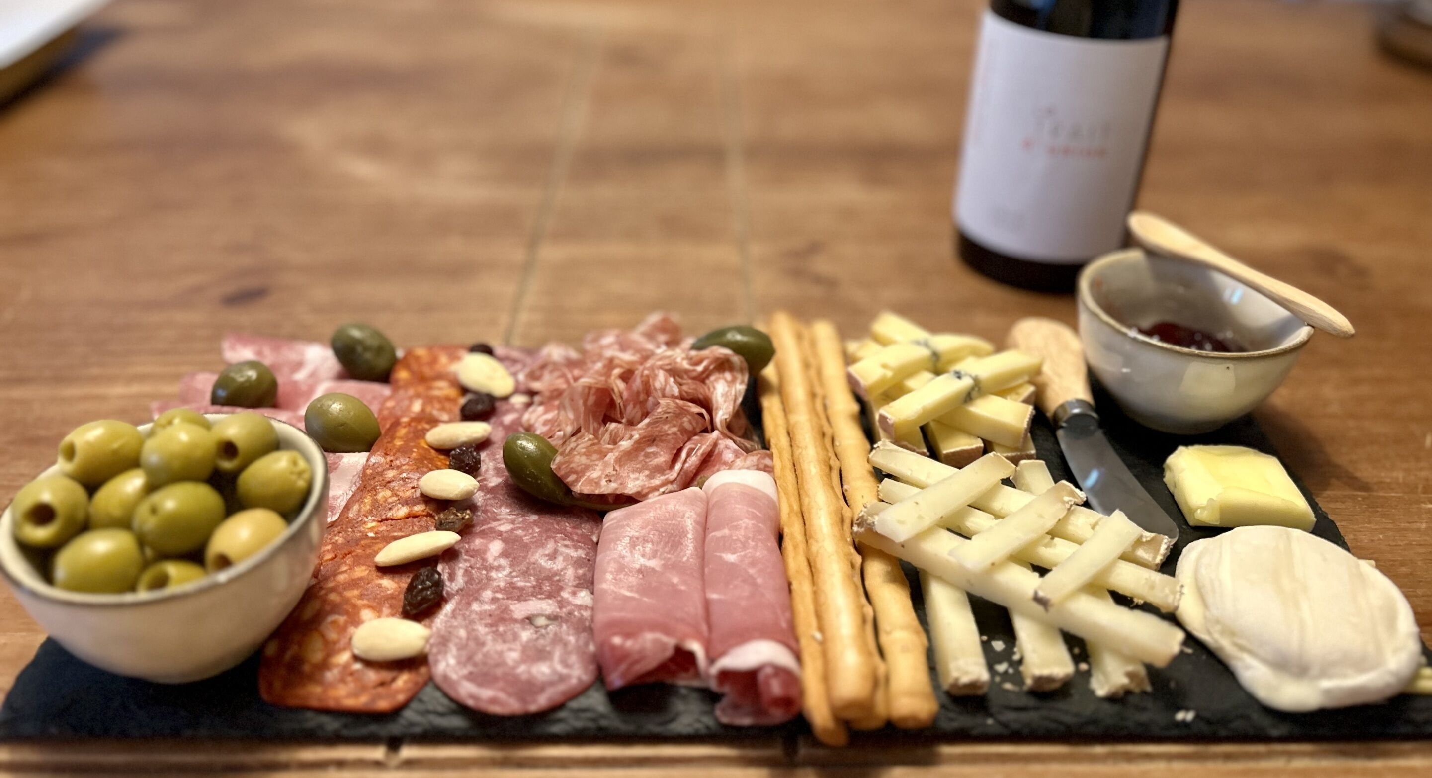 Una tabla de fiambres con diversos embutidos, quesos, aceitunas y galletas.