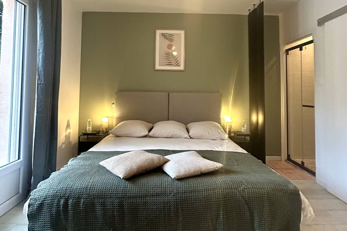 Une chambre d’hôtel avec un lit, un ventilateur de plafond, des lampes de chevet, un tableau encadré au mur et une fenêtre avec des rideaux.