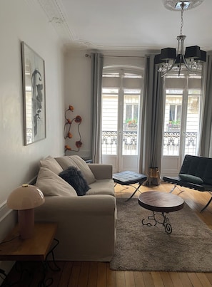 A living room with a sofa, a small table, a coffee table, a lamp, and a balcony with a view.