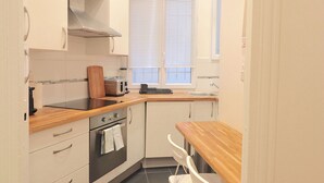 Cocina compacta con encimeras de madera, horno integrado, tostadora y ventana con persianas.