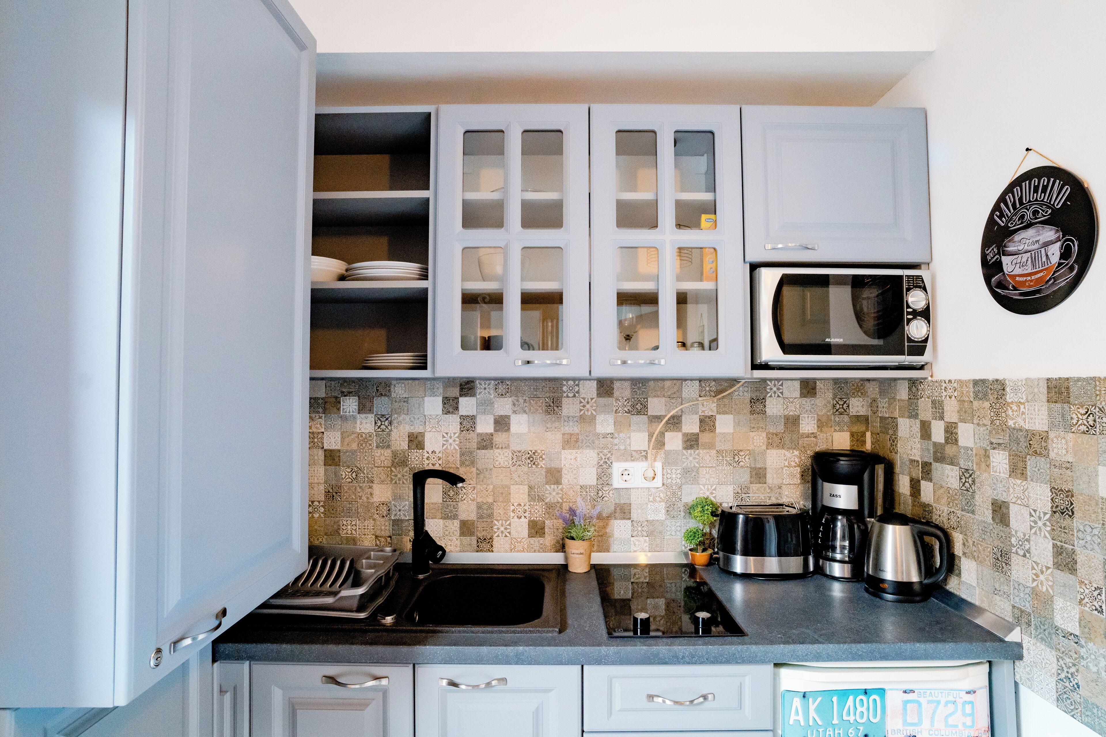 A kitchen with white cabinets, a microwave, a coffee maker, and a tiled backsplash.