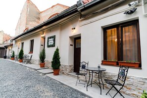 A building with a white facade, stone accents, and a tiled roof. There are outdoor seating areas with tables and chairs, and potted plants. - Galeria Grafit Apartments (Sibiu)