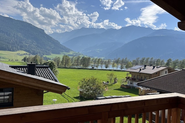 A view from a balcony overlooking a green valley, a lake, and mountains.