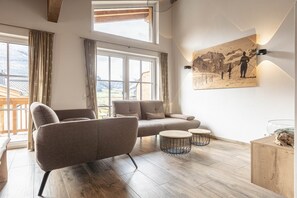 Una sala de estar moderna con un sofá, dos mesas redondas de centro y un cuadro de un paisaje montañoso.
