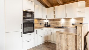 A modern kitchen with white cabinets, a wooden ceiling, and a built-in oven. - Superior Ferienhaus # 4B mit Sauna (Uttendorf)