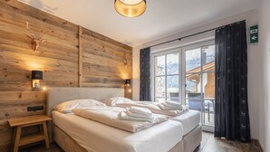 A bedroom with a wooden headboard, a bed with white linens, a bedside table, and a window with a view of a mountain landscape. - Superior Ferienhaus # 4B mit Sauna (Uttendorf)