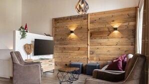 A modern living room with a wooden accent wall, a flat-screen TV, two armchairs, a coffee table, and a sofa.