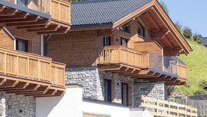 A multi-story wooden chalet with balconies, stone walls, and a sloped roof.