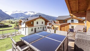 A wooden deck with solar panels, wicker furniture, and a view of snow-capped mountains.
