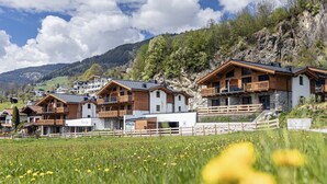 A row of chalet-style buildings with balconies, set against a mountainous backdrop.