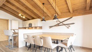A modern kitchen with wooden beams, a dining area with a long table and chairs, and a ski-themed wall decoration.