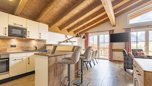 A modern kitchen with wooden beams, a bar area with stools, and a large window with a view.